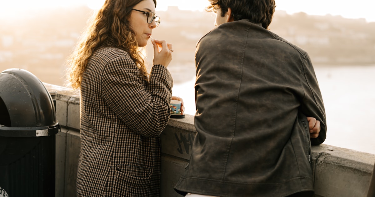 Una pareja conversando de frente al atardecer, con un café
