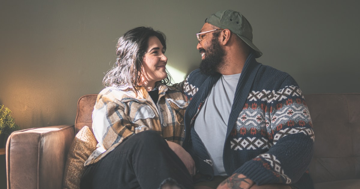 Una pareja mirándose y sonriendo, sentada en el sillón