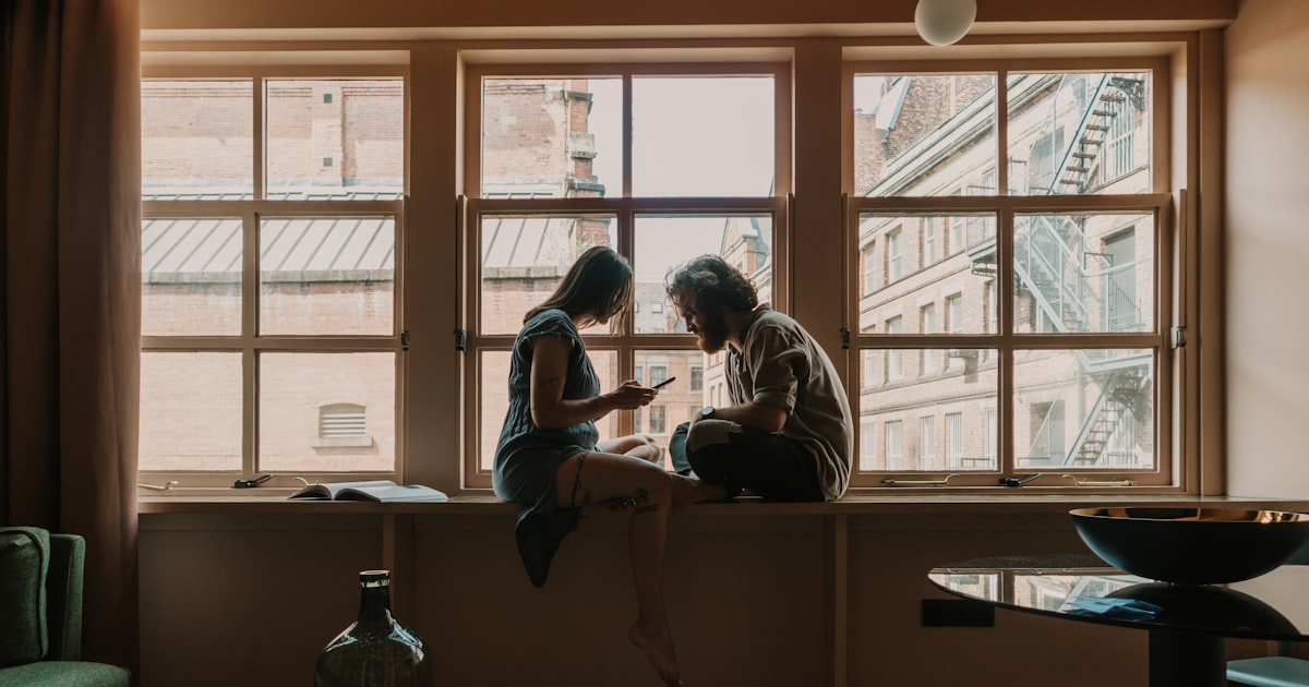 Una pareja sentada junto a una ventana con luz cálida, conversando