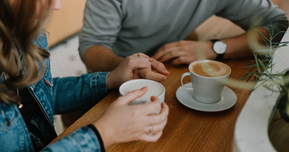 Una pareja tomada de la mano sobre una mesa, con dos cafés